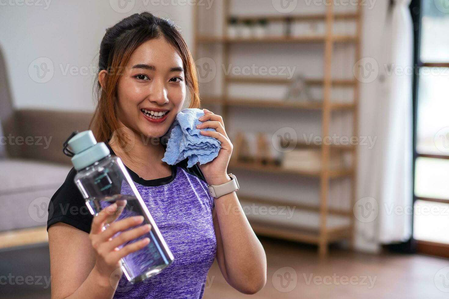 Asian woman taking break after exercise with drinking water at the home. home exercise concept. photo