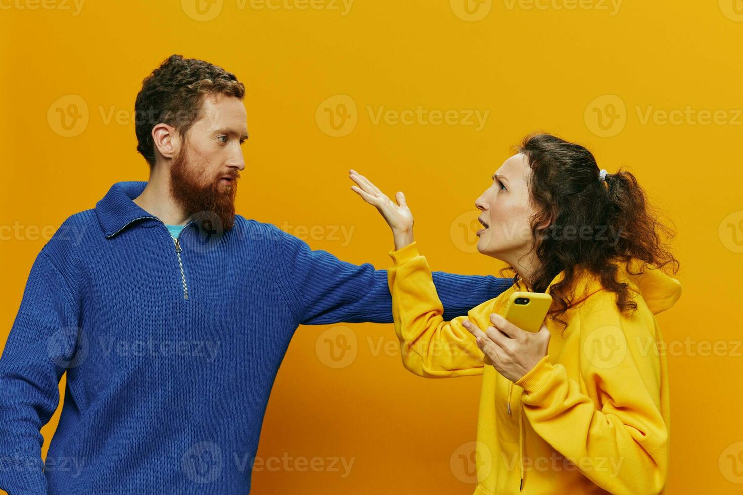 Woman man cheerful couple with phones in hand social networking and communication crooked smile fun and fight, in yellow background. The concept of real family relationships, freelancers, work online. photo