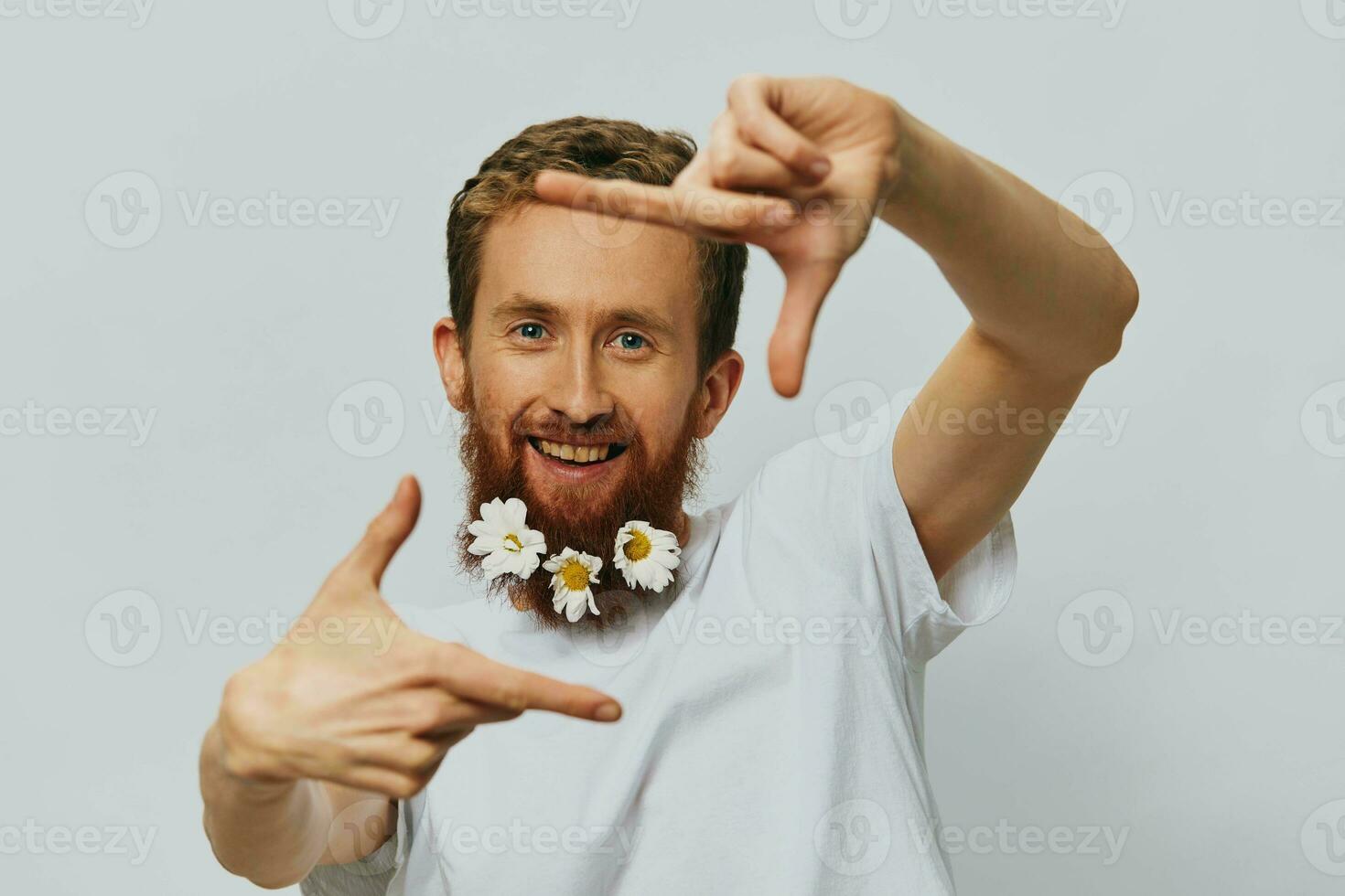 Portrait of a funny man in a white T-shirt with flowers daisies in his beard on a white isolated background, copy place. Holiday concept and congratulations. photo