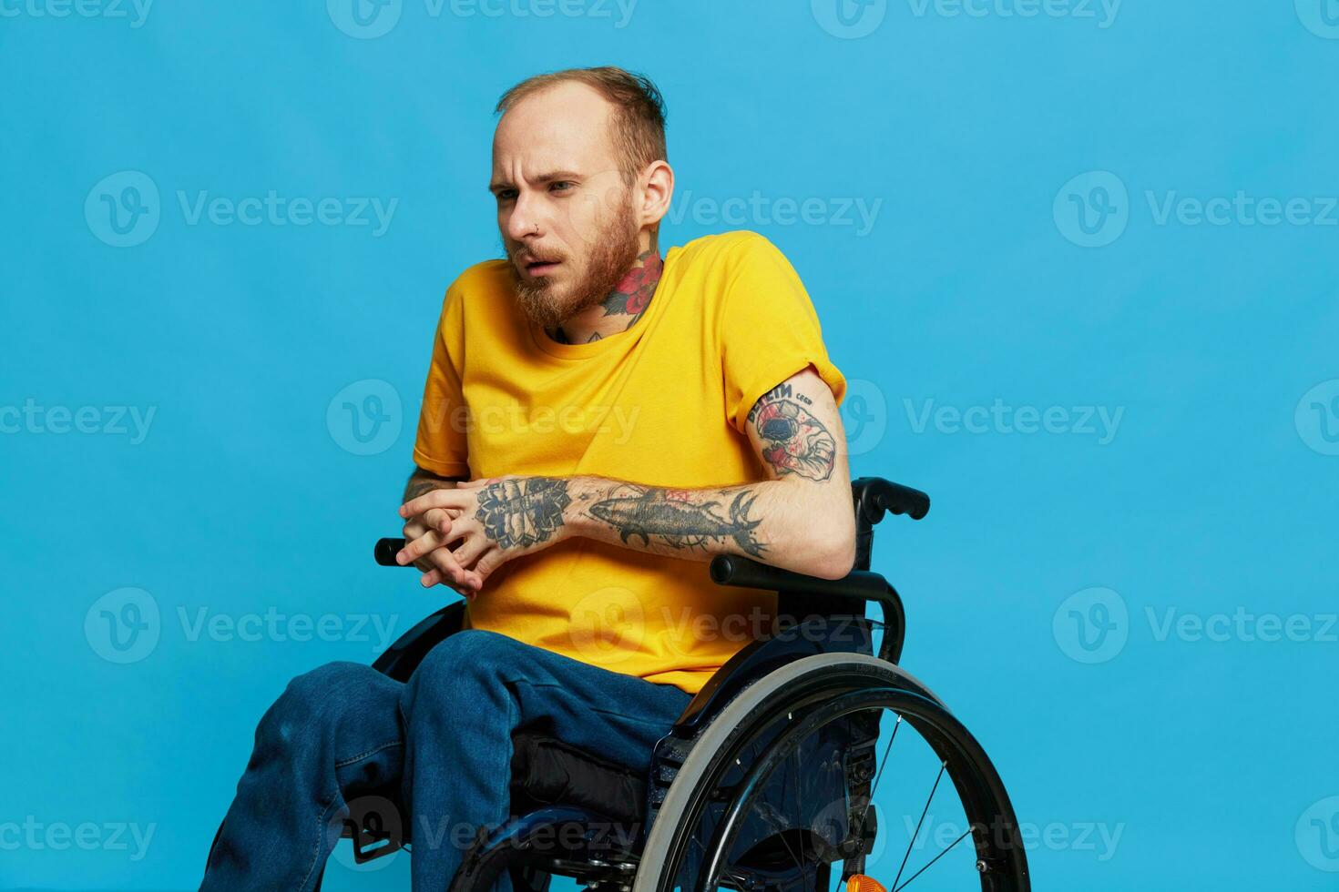 a man sits in a wheelchair in a t-shirt on a blue background in the studio, the concept of a free barrier-free environment for people with disabilities photo