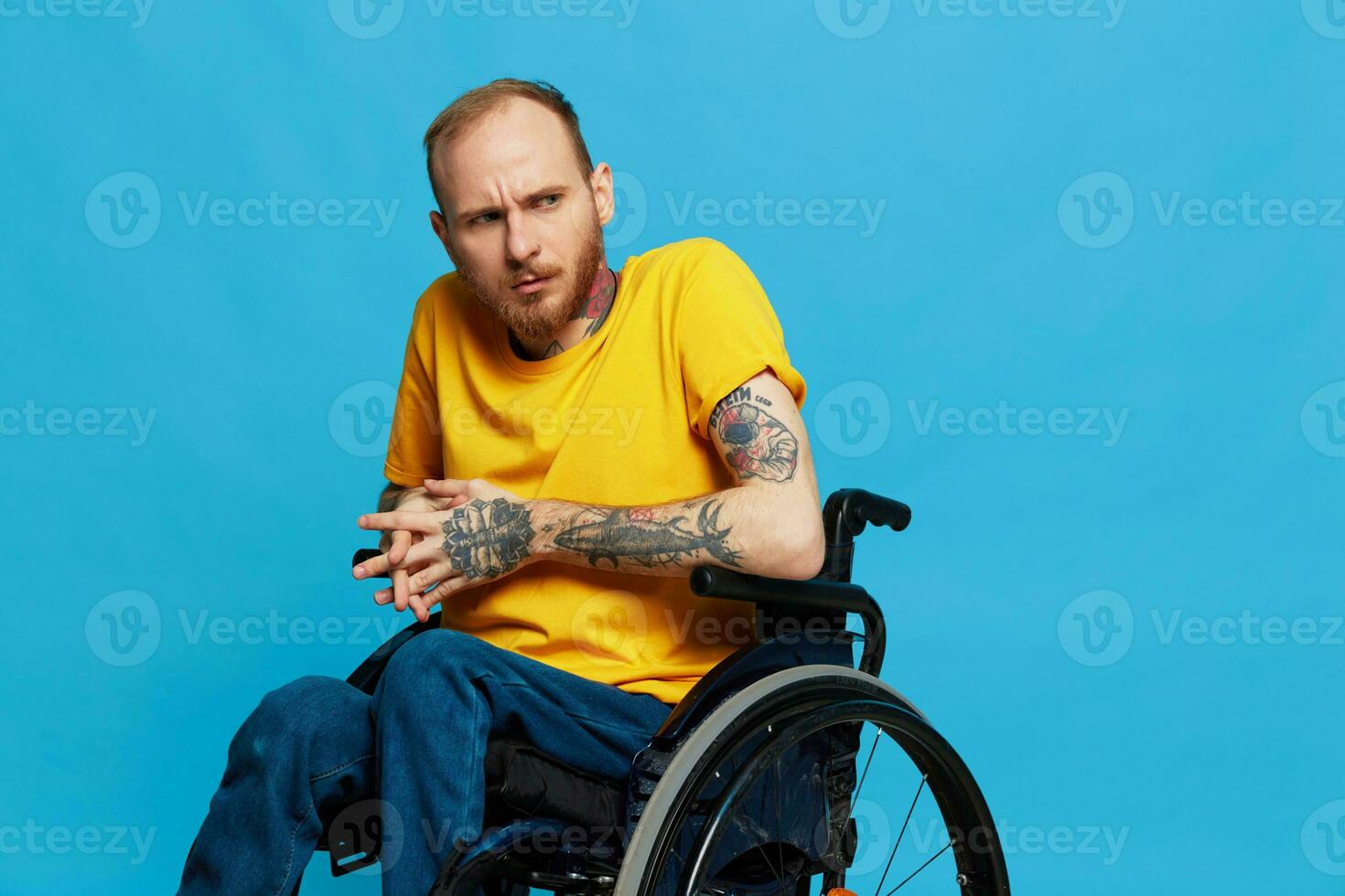 a man sits in a wheelchair in a t-shirt on a blue background in the studio, the concept of a free barrier-free environment for people with disabilities photo