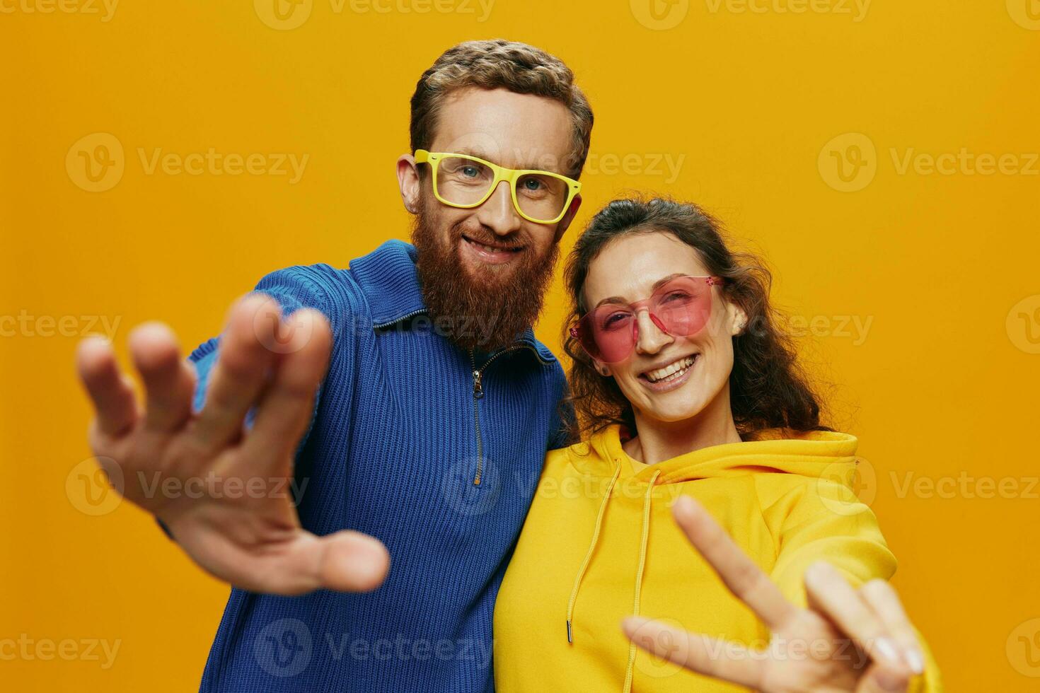 Man and woman couple smiling cheerfully and crooked with glasses, on yellow background, symbols signs and hand gestures, family shoot, newlyweds. photo