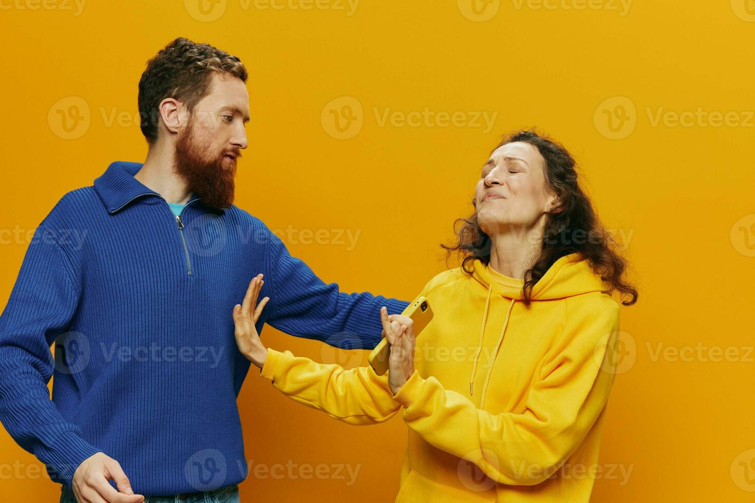 Woman man cheerful couple with phones in hand social networking and communication crooked smile fun and fight, in yellow background. The concept of real family relationships, freelancers, work online. photo