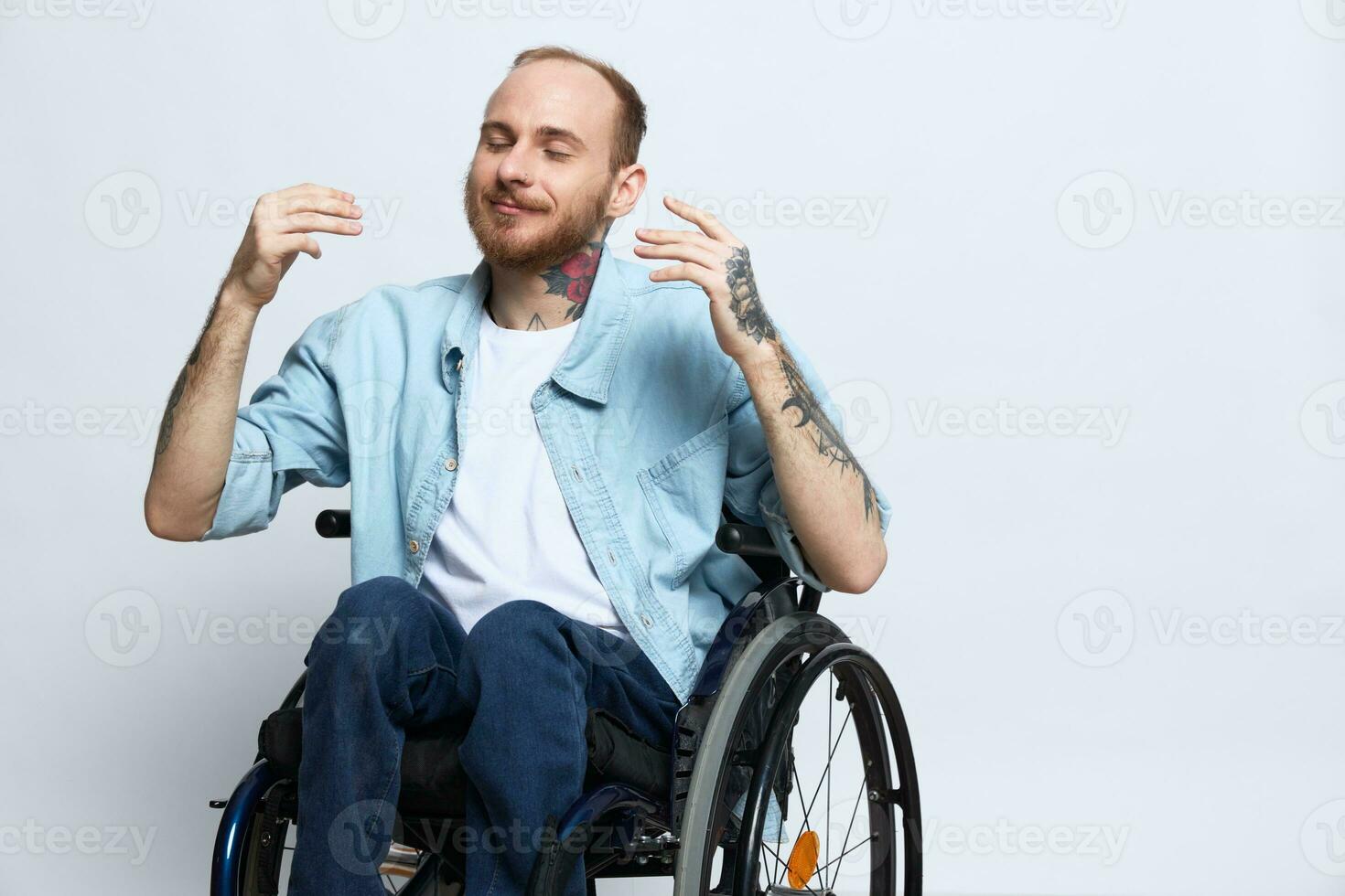 A man in a wheelchair smile, copy space, with tattoos on his arms sits on a gray studio background, the concept of health is a person with disabilities, a real person photo