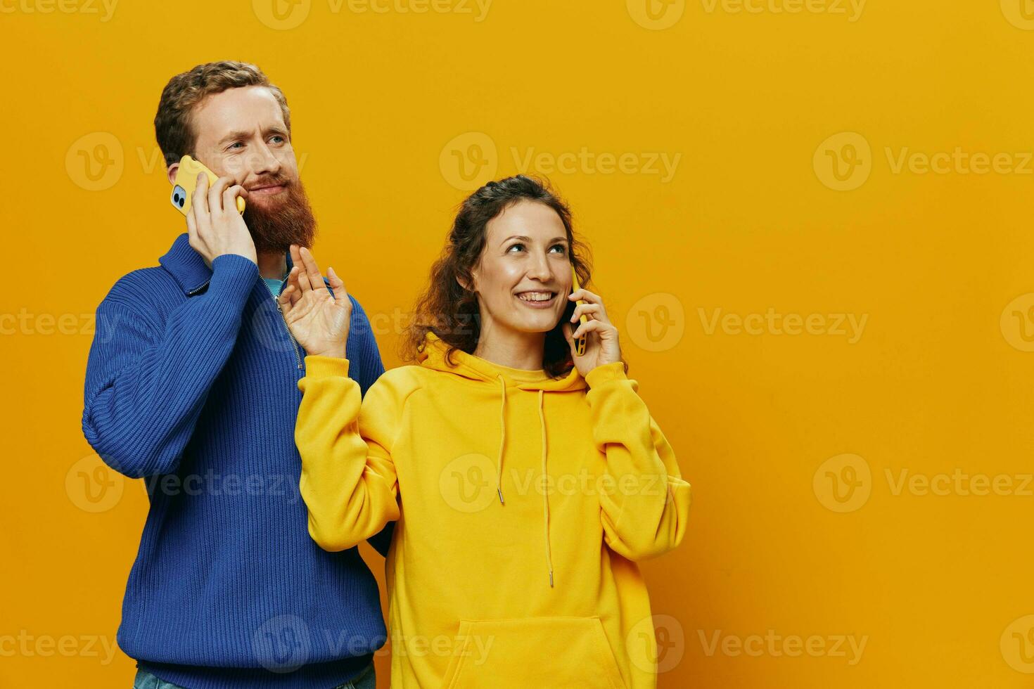 Woman and man cheerful couple with phones in hand talking on cell phone crooked smile cheerful, on yellow background. The concept of real family relationships, talking on the phone, work online. photo