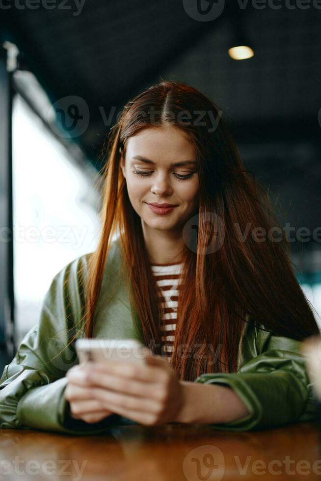 A woman freelance blogger sitting in a cafe with a phone in her hands typing a message and smiling, a hipster girl photo