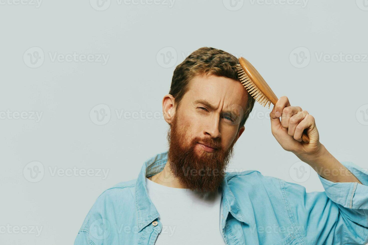 Portrait of a man with a massage comb in his hands, combing his hair and beard, hair loss problem photo