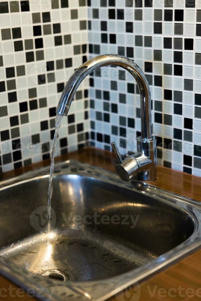 Clean sink with pouring water in the kitchen, metal faucet and sink in an old home interior. photo