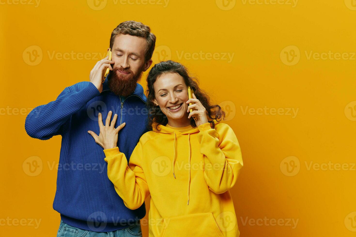 Woman and man cheerful couple with phones in hand talking on cell phone crooked smile cheerful, on yellow background. The concept of real family relationships, talking on the phone, work online. photo