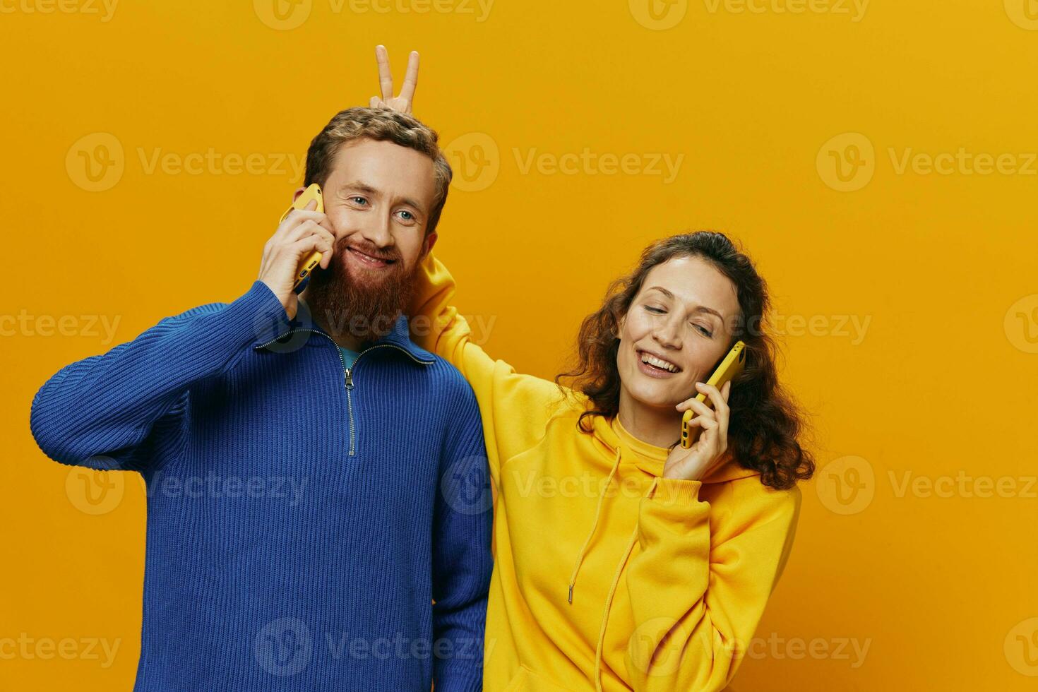 Woman and man cheerful couple with phones in hand talking on cell phone crooked smile cheerful, on yellow background. The concept of real family relationships, talking on the phone, work online. photo