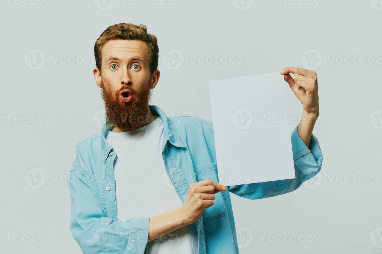 Portrait of an adult male on a gray background with a white sheet of paper in his hands for your design and text, layout, copy space, space for text, finger pointing photo