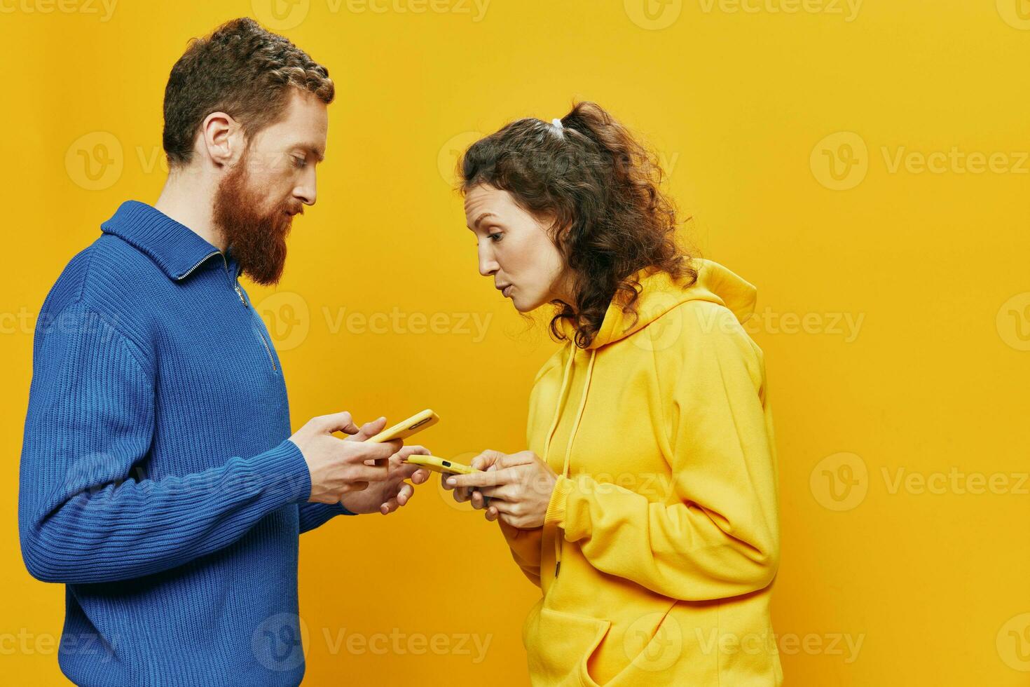 Woman man cheerful couple with phones in hand social networking and communication crooked smile fun and fight, in yellow background. The concept of real family relationships, freelancers, work online. photo