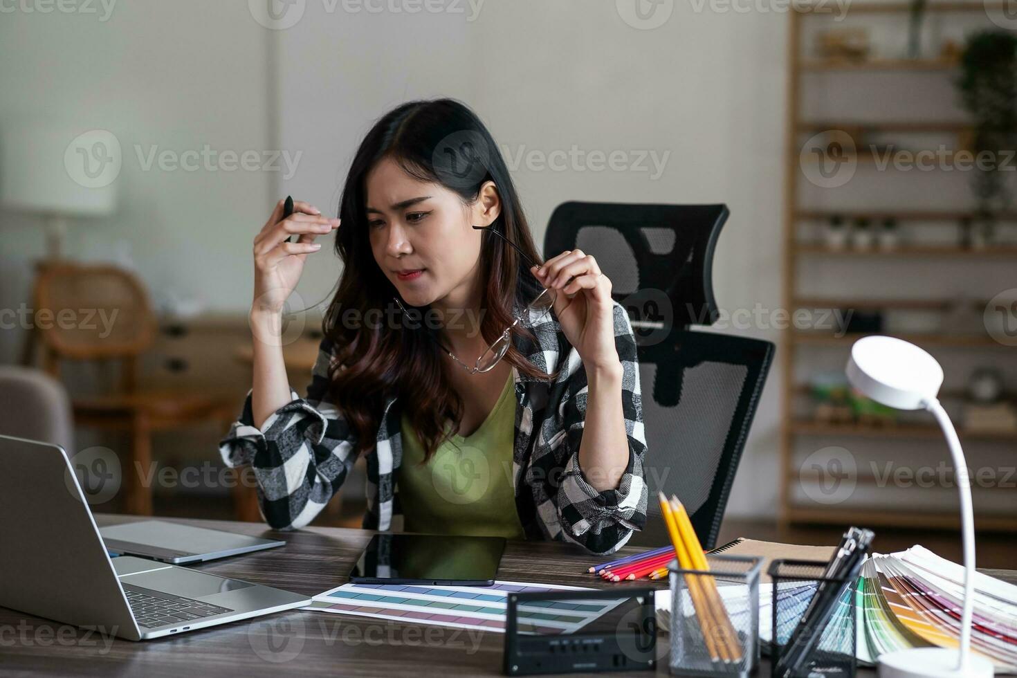 Serious and focused female graphic designer sitting at her desk, surrounded by sketches and drawings. photo