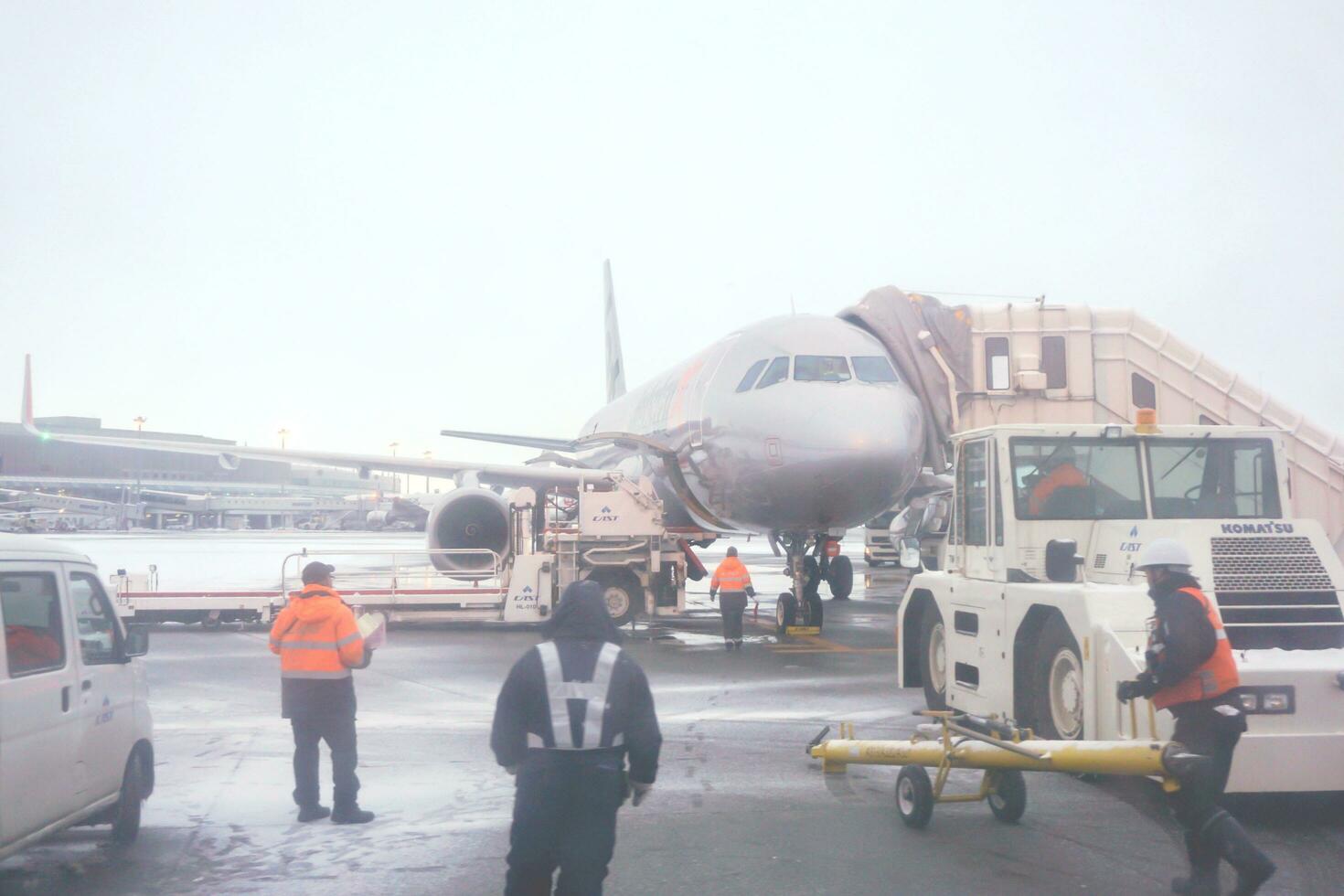 Chitose, Hokkaido, Japan, 2018 - Airplane of jet star's airline with Jet bridge parked on airport ground and airline staff on winter sky background. photo