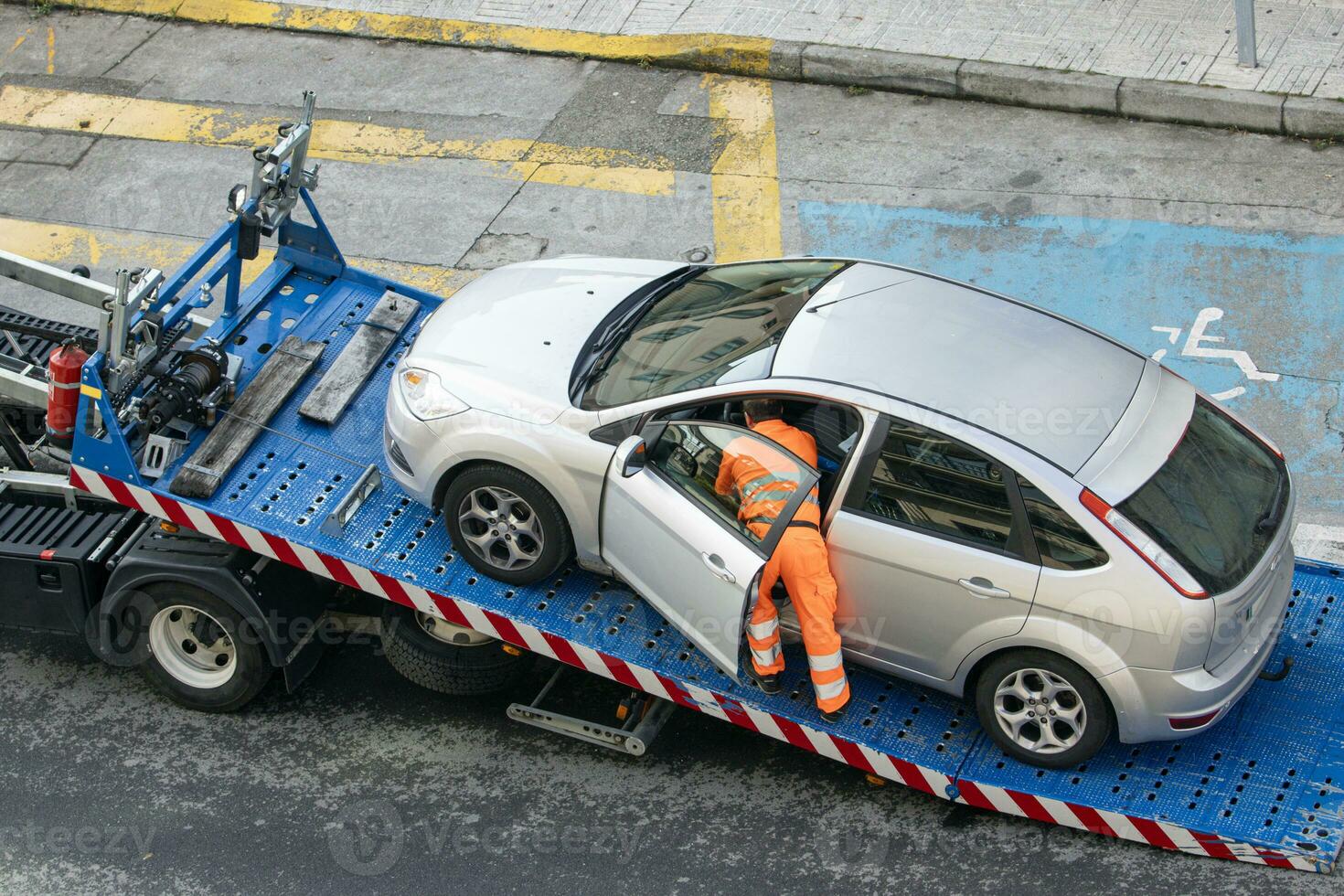 Damaged car being loaded onto tow truck by a worker. Towing service on the city. Roadside assistance concept photo