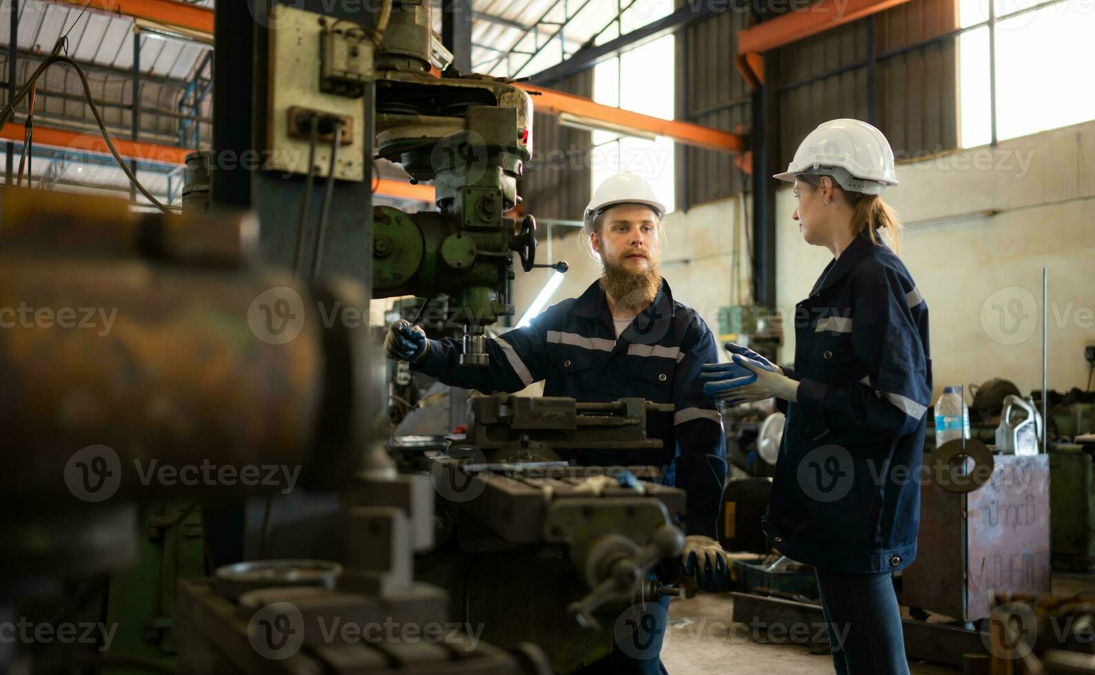 Both of mechanical engineers are checking the working condition of an old machine that has been used for some time. In a factory where natural light shines onto the workplace photo
