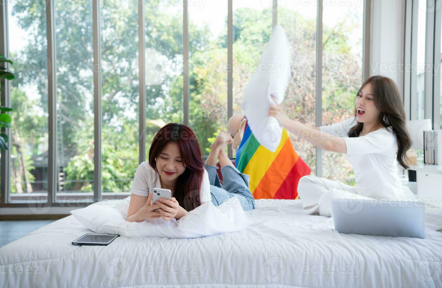 When an LGBT couple arrives in their hotel room they playfully hit each other on the bed with pillows. before going out to see the nature of the countryside photo