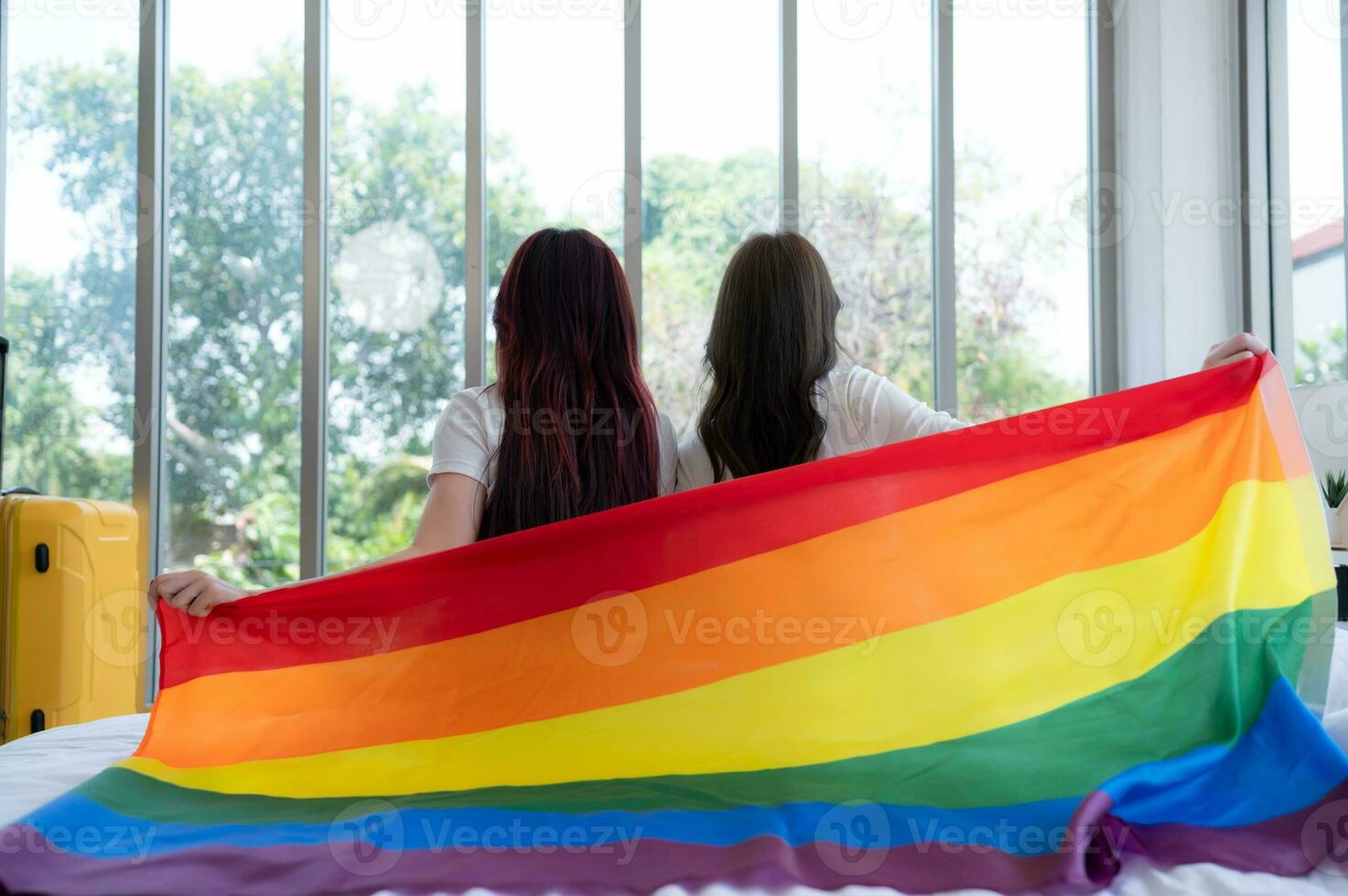 The LGBT couple sat on the bed, covered in rainbow flags, peering out the window to observe the nature in the hotel room. photo