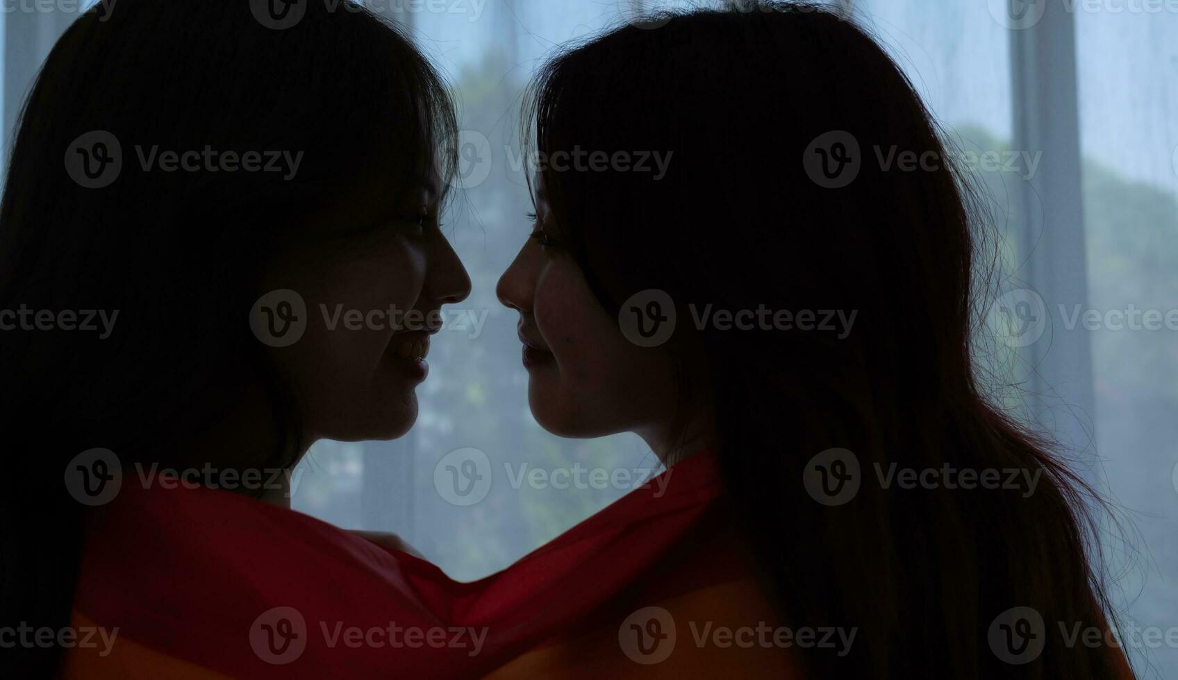 The LGBT couple sat on the bed, covered in rainbow flags, peering out the window to observe the nature in the hotel room. photo