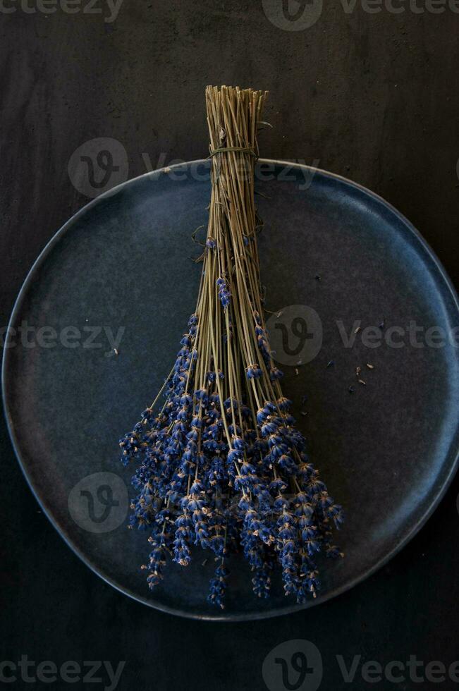 A bouquet of dry lavender flowers lies on a plate on a dark background photo
