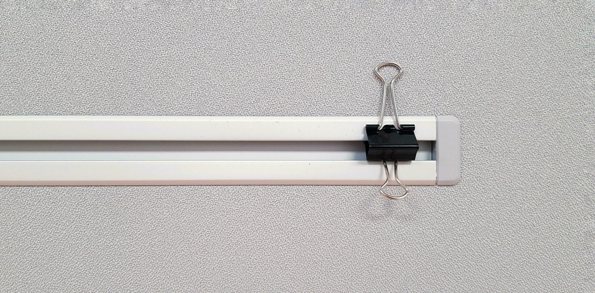 Black paper clip on gray plastic or fiberglass partition wall with copy space. Minimal object and Art concept photo