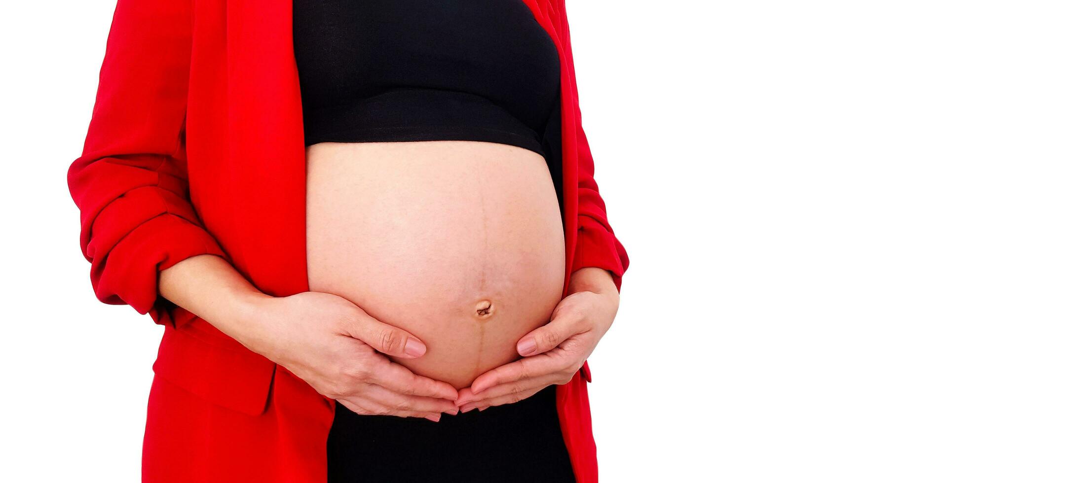 cerca arriba embarazada mujer vistiendo rojo traje sostiene manos en hinchado barriga aislado en blanco antecedentes y Copiar espacio con recorte camino. el embarazo 7-9 meses, maternidad, amar, expectativa y coche foto