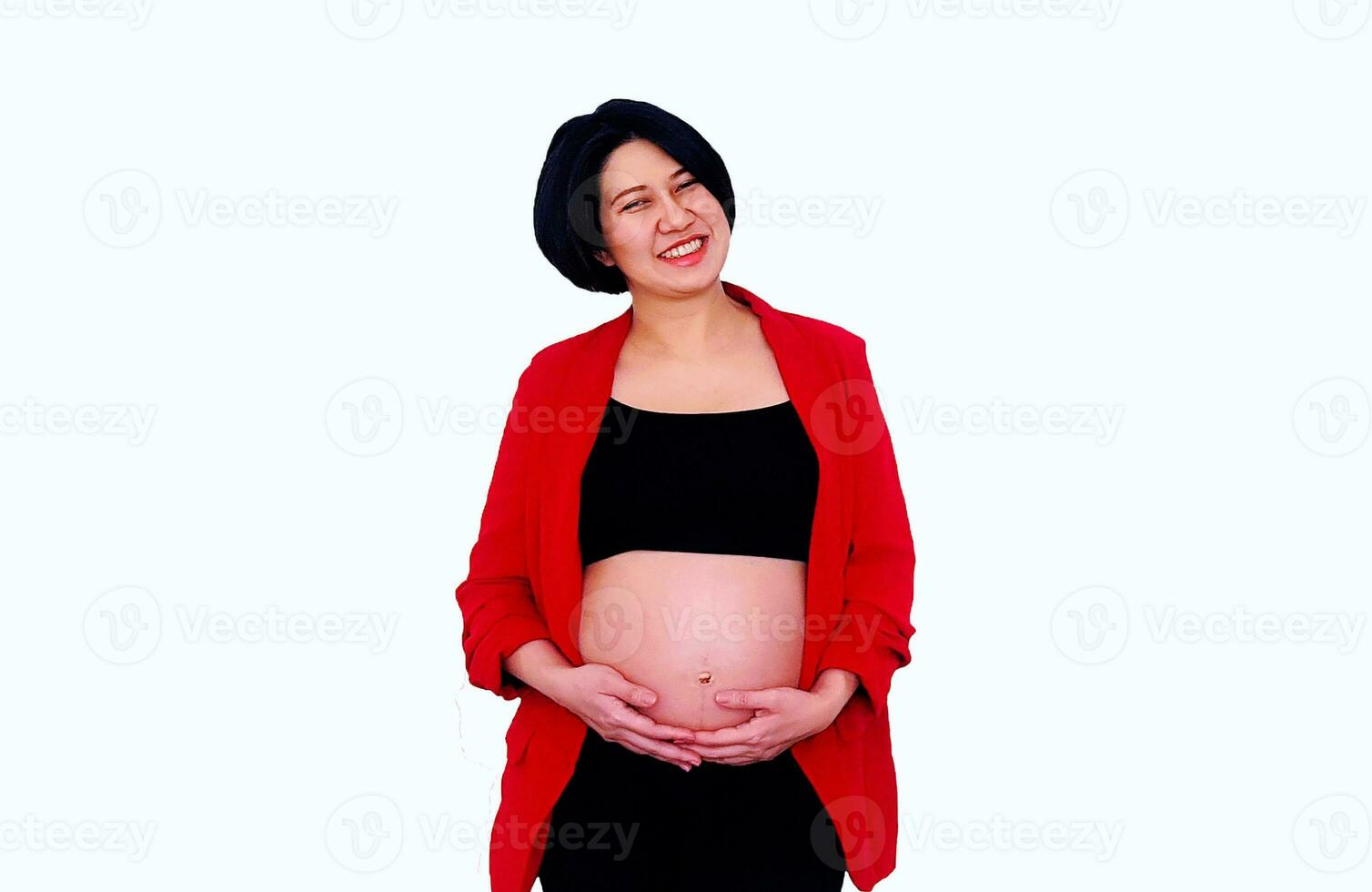 Pretty pregnant woman wearing suit, standing, smiling and touching or holding her belly isolated on white background with clipping path. Pregnancy 7-8 months, motherhood, love, expectation and care photo