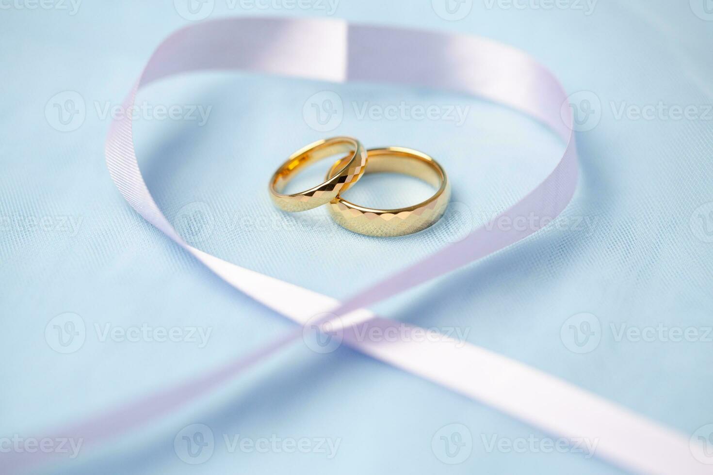 Golden wedding rings for engagement. Marriage golden rings with white, pink ribbons background. Rings on the white and red rose. The marriage rings is the symbol of traditional wedding of pair lovers. photo