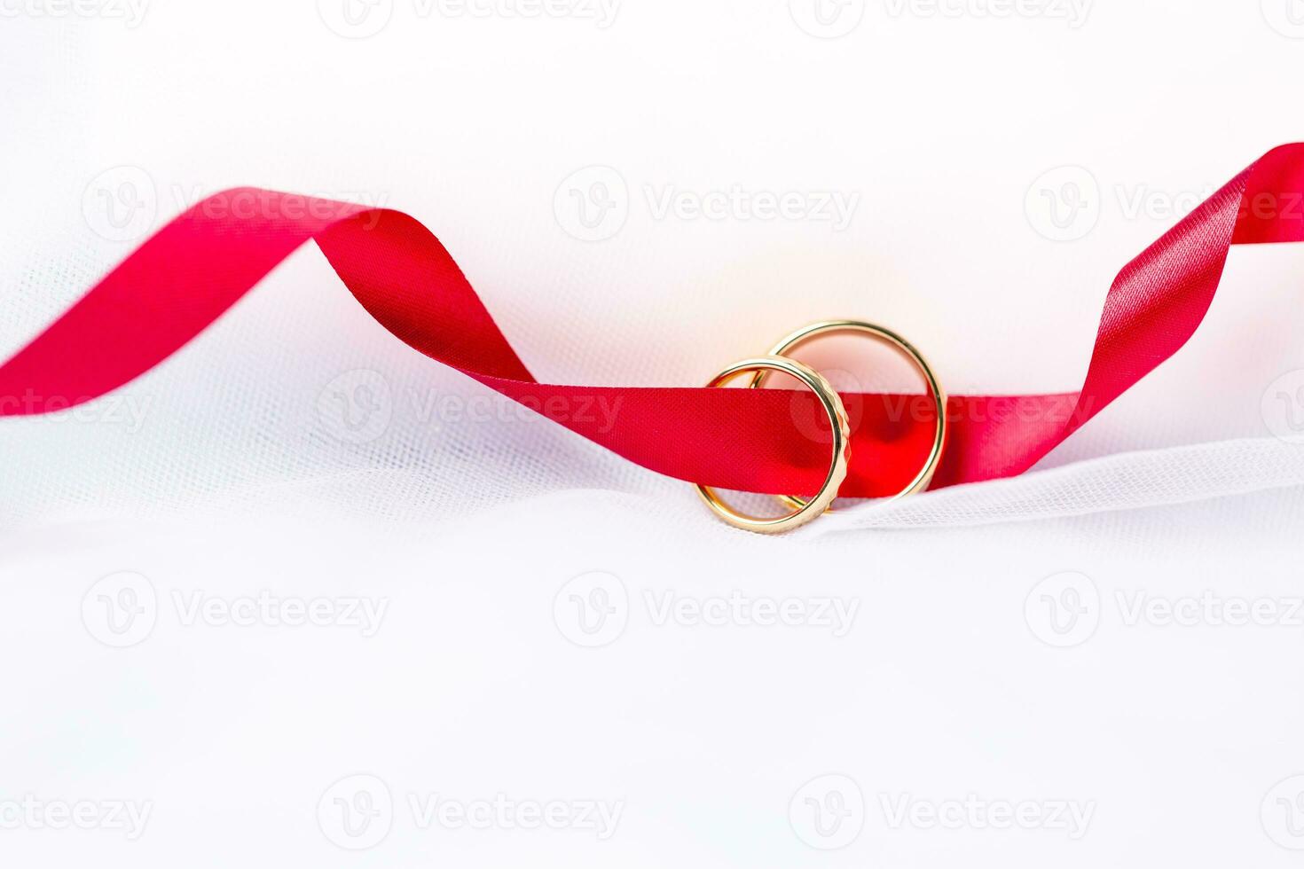 Golden wedding rings for engagement. Marriage golden rings with white, pink ribbons background. Rings on the white and red rose. The marriage rings is the symbol of traditional wedding of pair lovers. photo