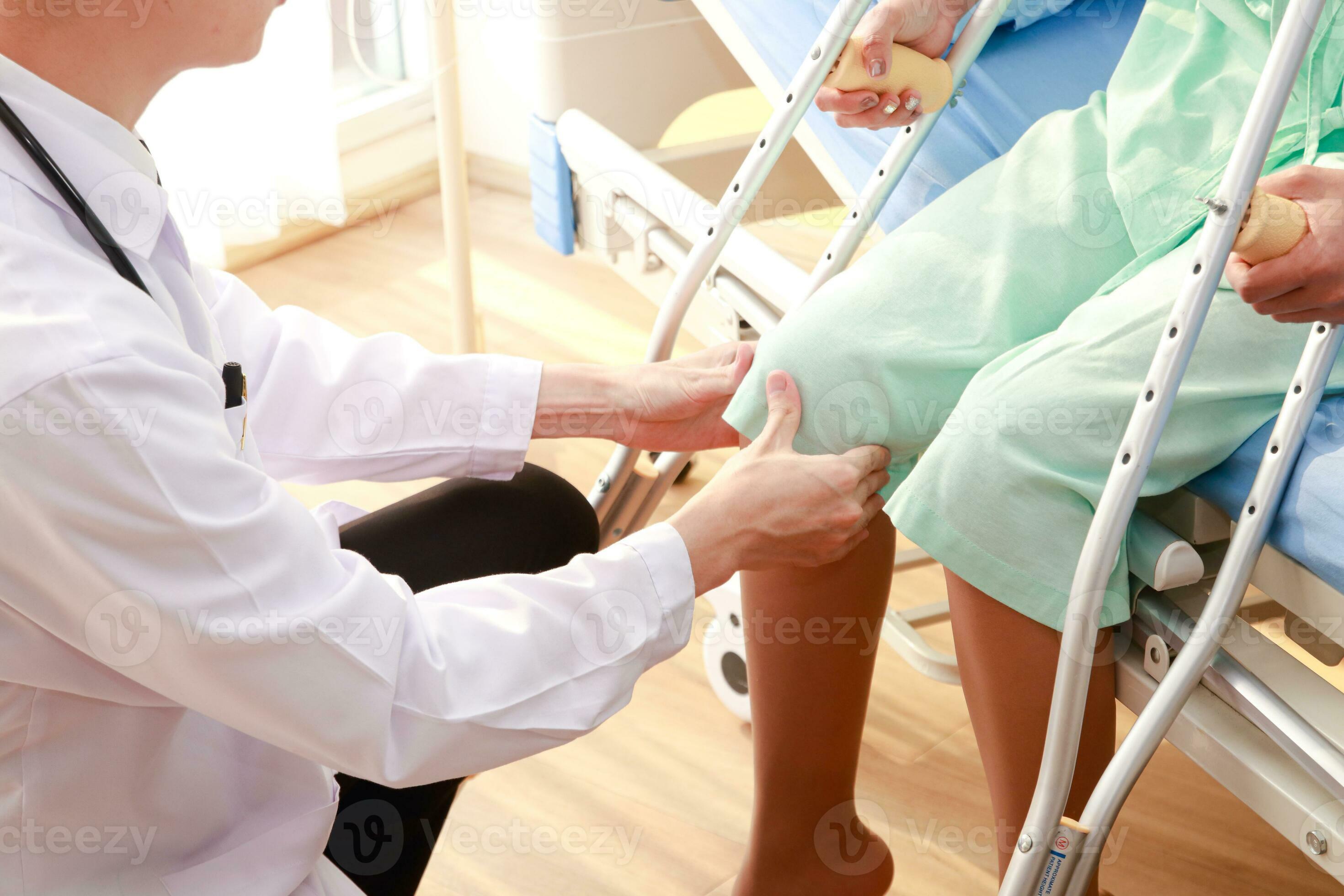 Asian male doctor examining knee of female patient sitting on nursing