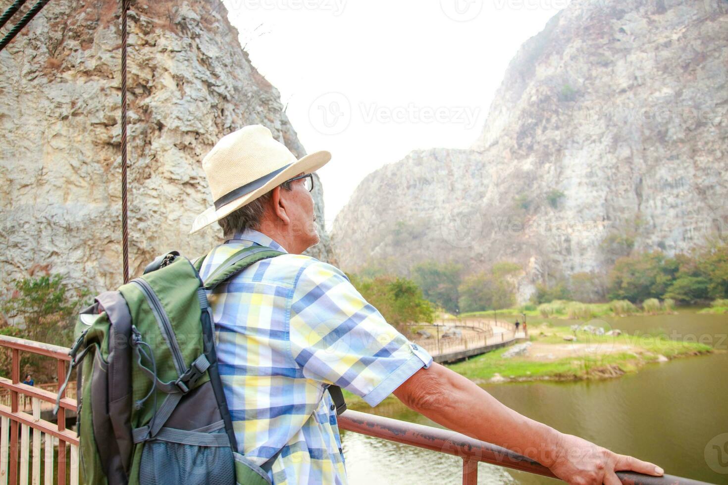 Asian elderly man carrying a backpack to travel to nature Stand and look at the view of the rocky mountains. Travel concept, happy retirement life, health care photo