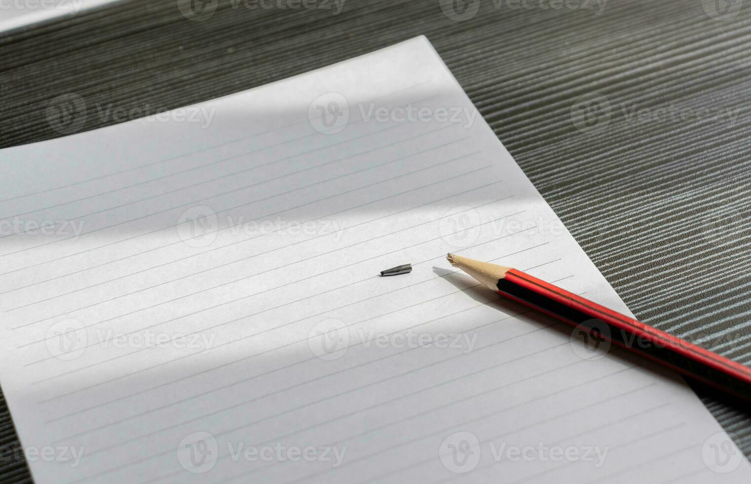 Broken pencil and a blank paper on a wooden textured table with partial shadows, after some edits. photo