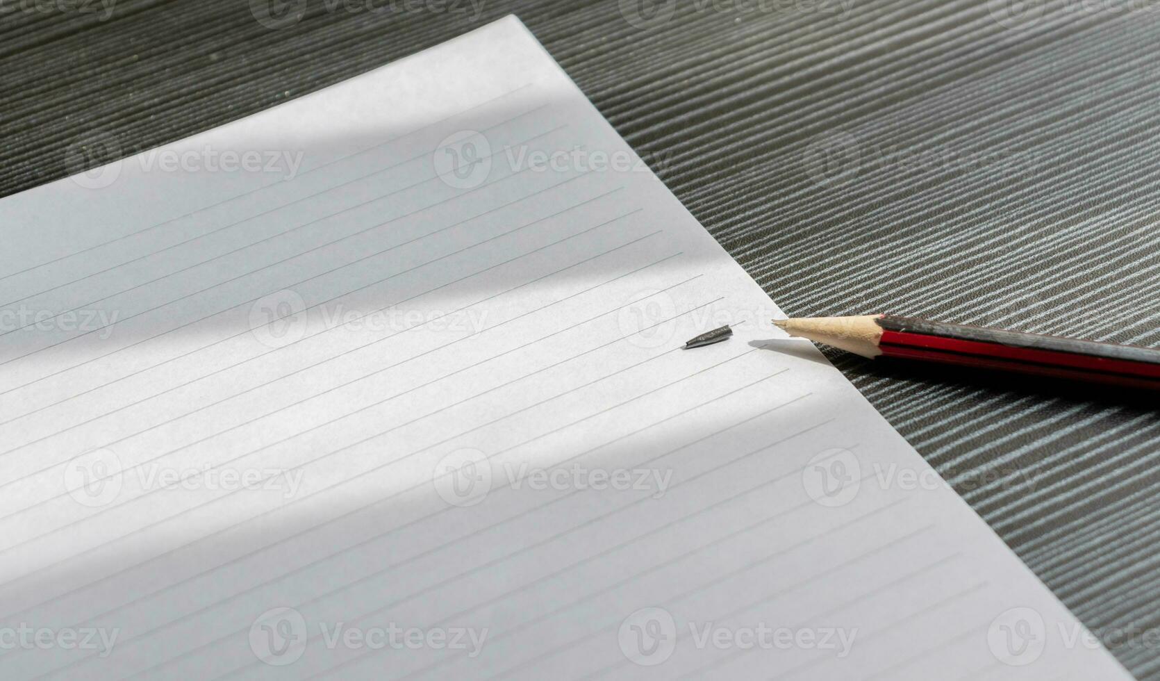 Broken pencil and a blank paper on a wooden textured table with partial shadows, after some edits. photo