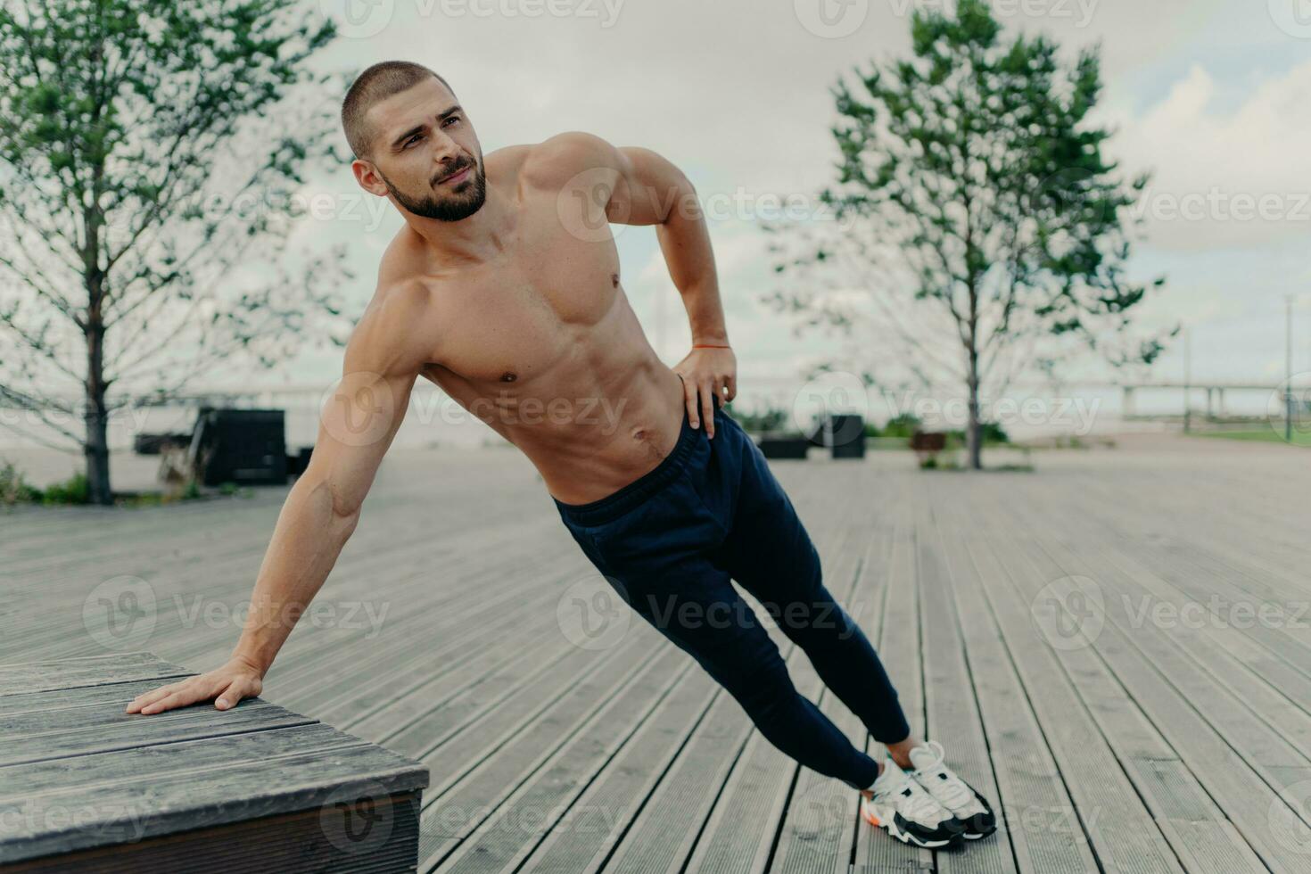 Shirtless bearded man  side plank, endurance, good shape. Active outdoor training, sportswear. photo