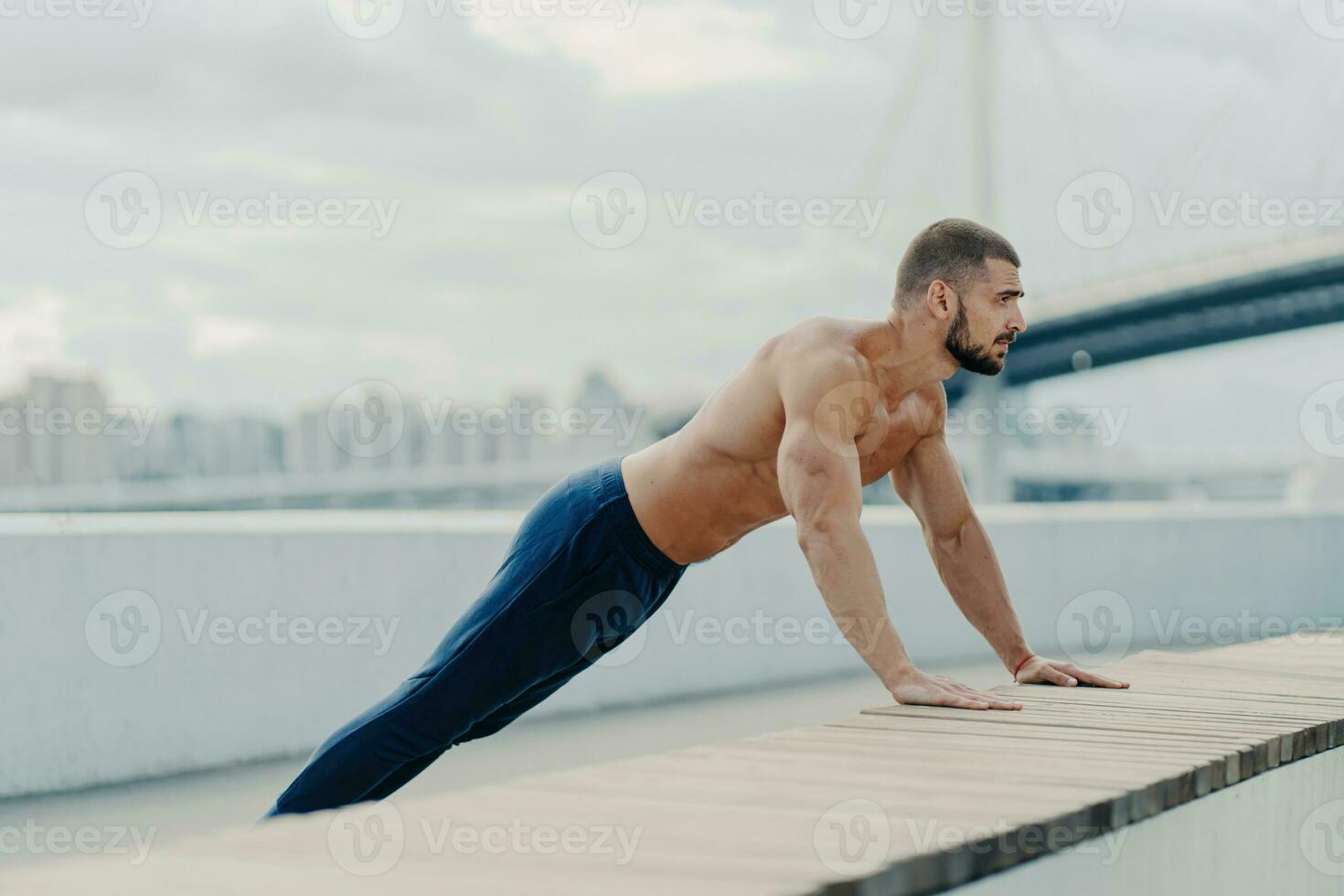 Athlete in plank pose does push-ups outdoors, breathes fresh air. Strong body, naked torso. Motivated to stay fit and lead an active, healthy lifestyle. Sports training. photo