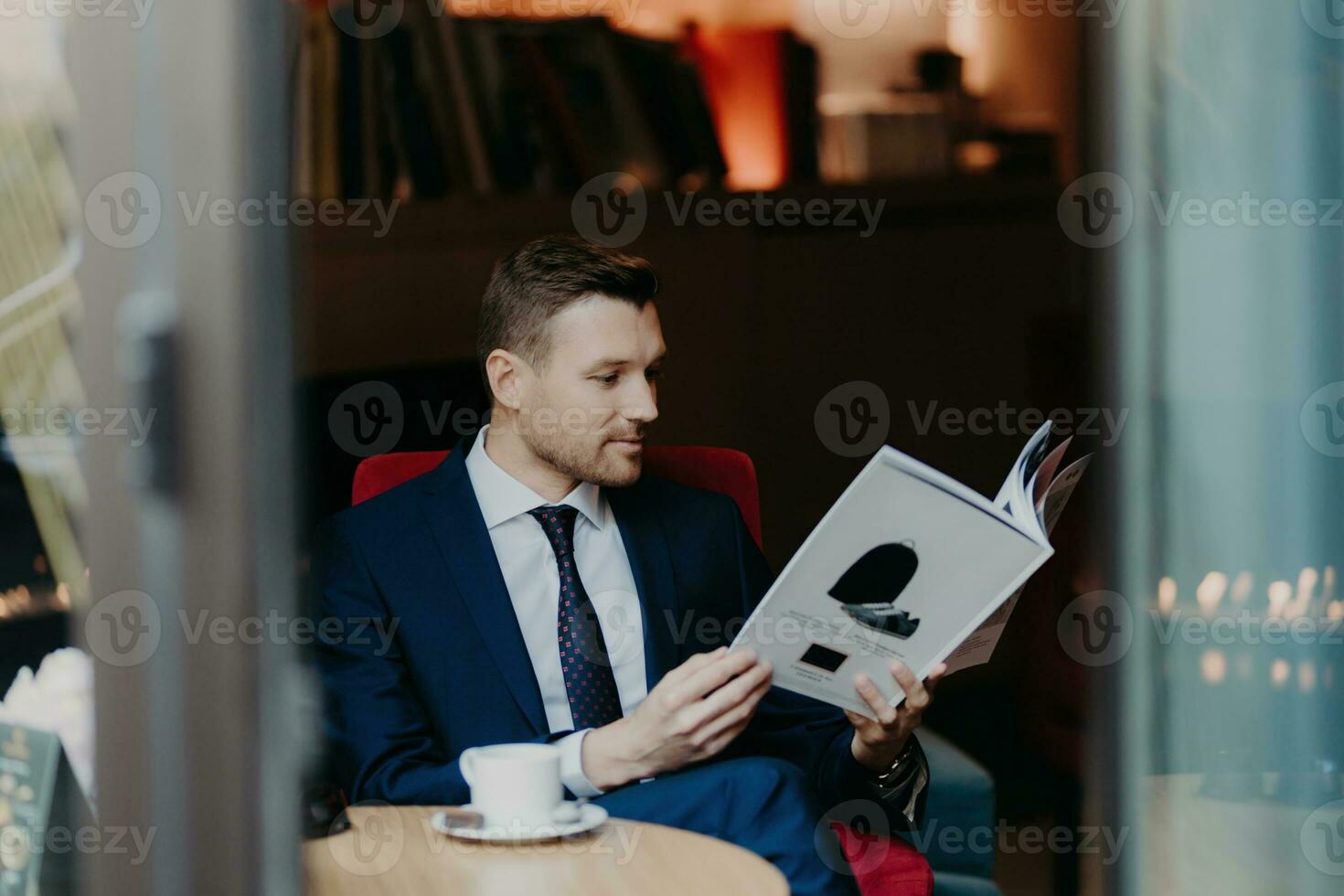 Successful businessman in coffee shop, focused on magazine, drinks hot