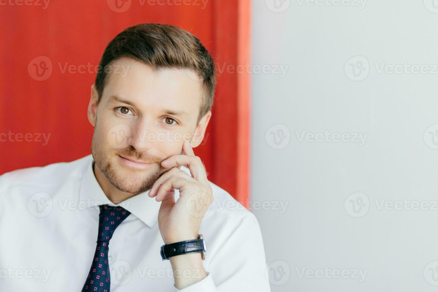 Confident office worker in white shirt with tie, hand on cheek, contemplates new stage in life. Poses against red and white background. Business concept. photo