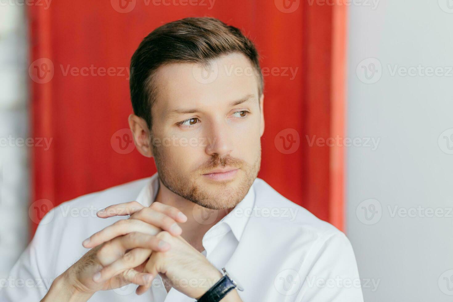 Pensive male worker, red background, deep in thoughts after meeting, owns big company. photo