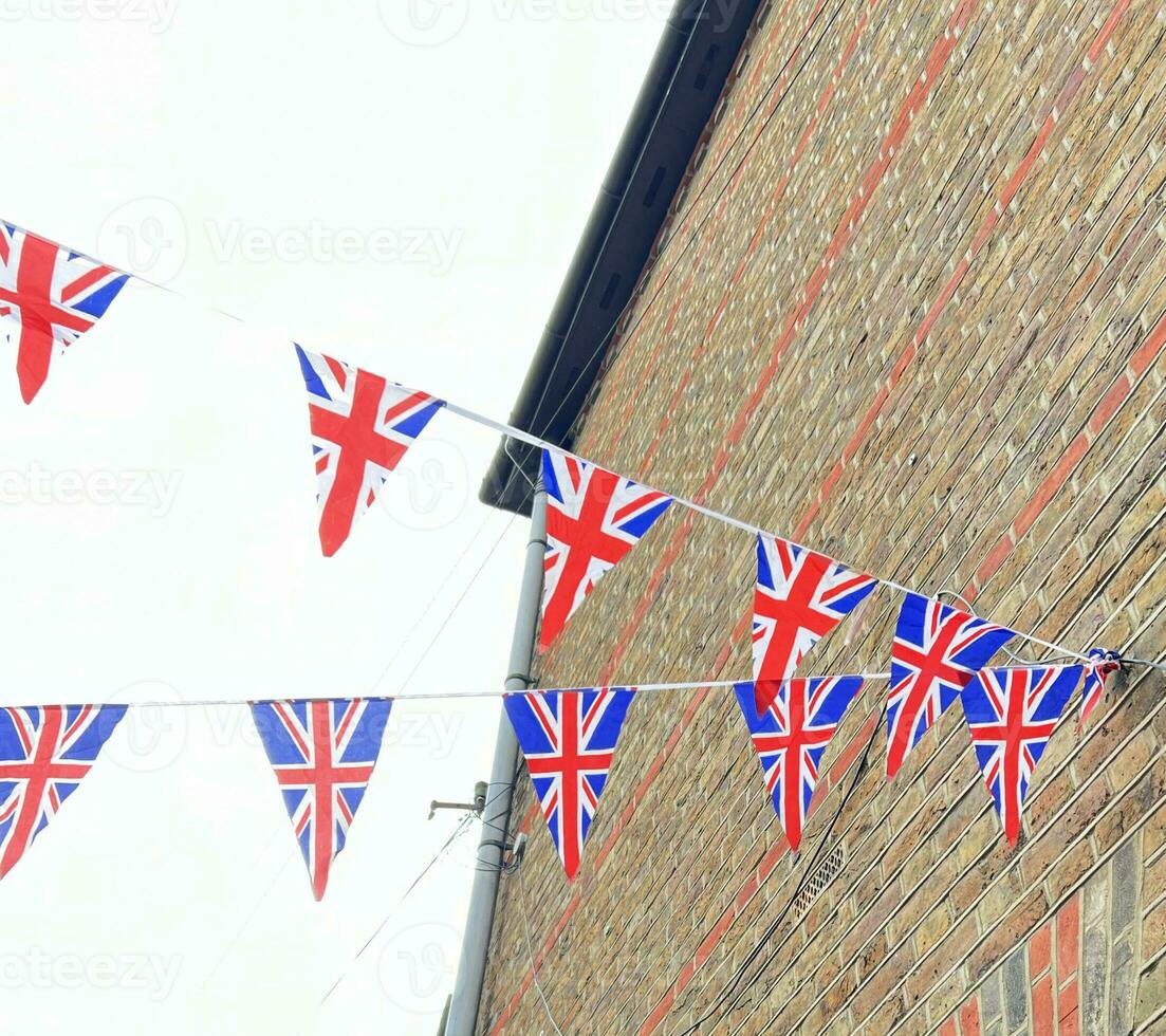 British Union Jack flags hanging at the street against brick wall, ready to national holiday celebration. Street party decorations in the UK city. photo