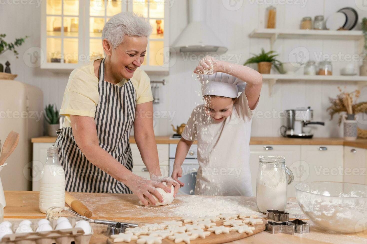 Happy family in kitchen. Grandmother and granddaughter child cook in kitchen together. Grandma teaching kid girl knead dough bake cookies. Household teamwork helping family generations concept. photo