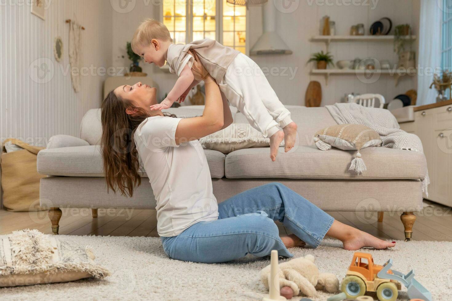 Happy family at home. Mother lifting in air little toddler child son. Mom and baby boy playing having fun together at home. Mother hugs baby with love care. Young mother kid son rest in living room. photo