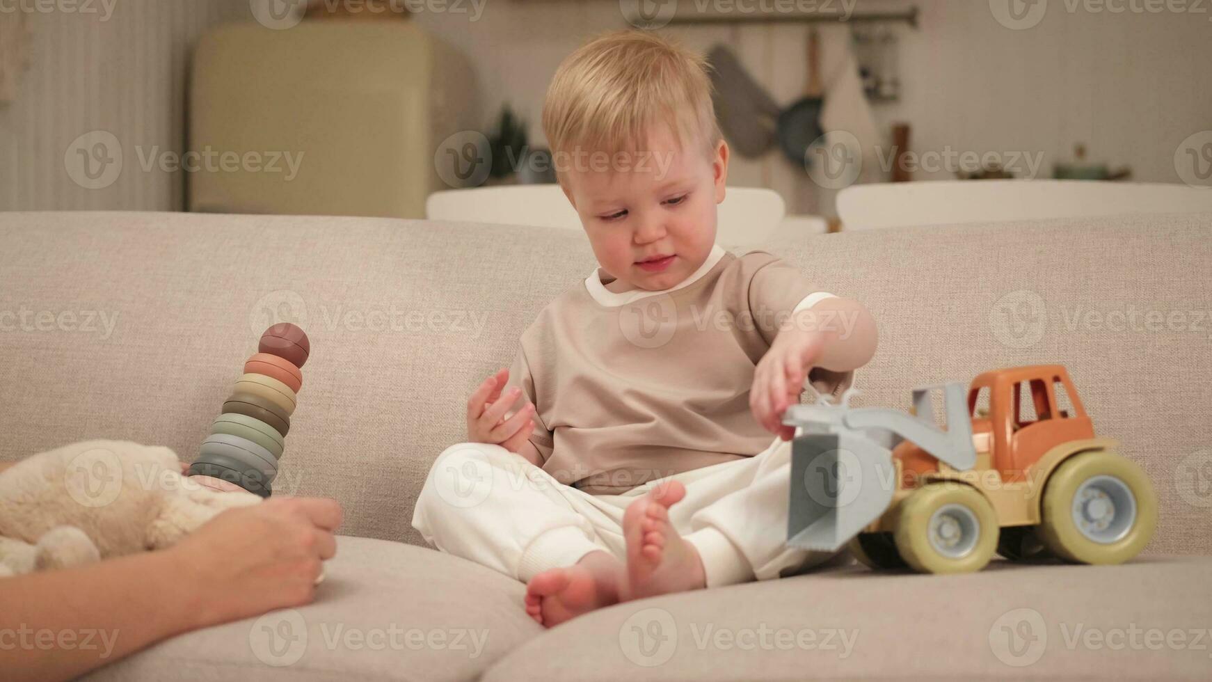 Happy family at home. Mother and baby boy playing with toys in couch at home indoors. Little toddler child and babysitter nanny having fun together. Young woman mom kid son rest in living room. photo