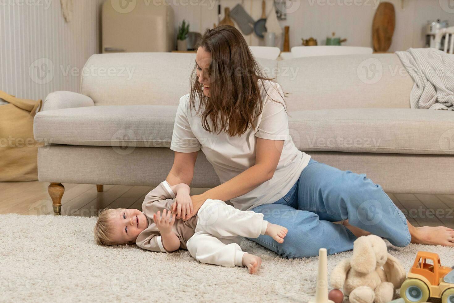 Happy family at home. Mother and baby boy playing with toys at home indoors. Little toddler child and babysitter nanny having fun together. Young woman mom kid son rest in living room. photo