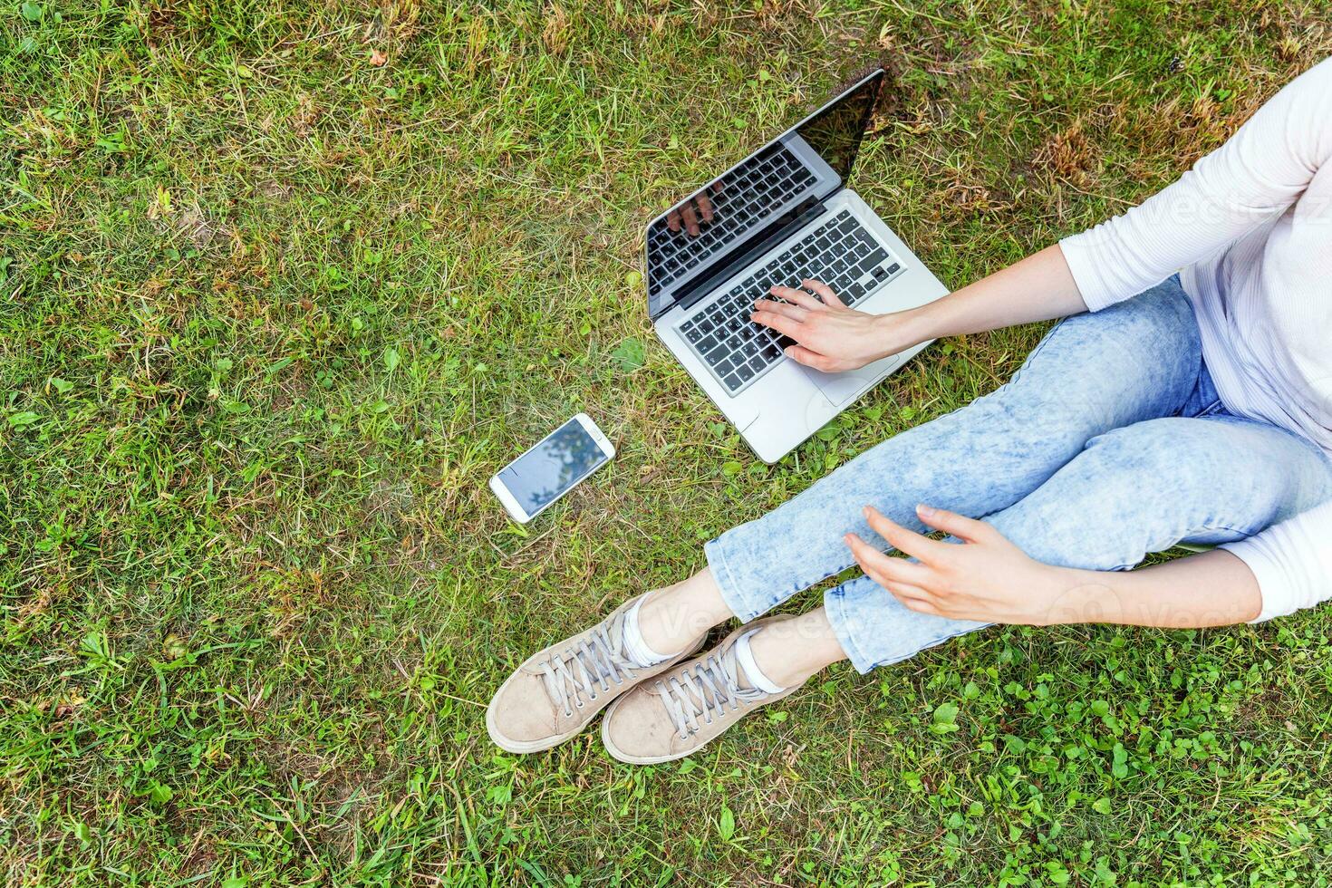 Woman legs on green grass lawn in city park, hands working on laptop pc computer. Freelance business concept photo