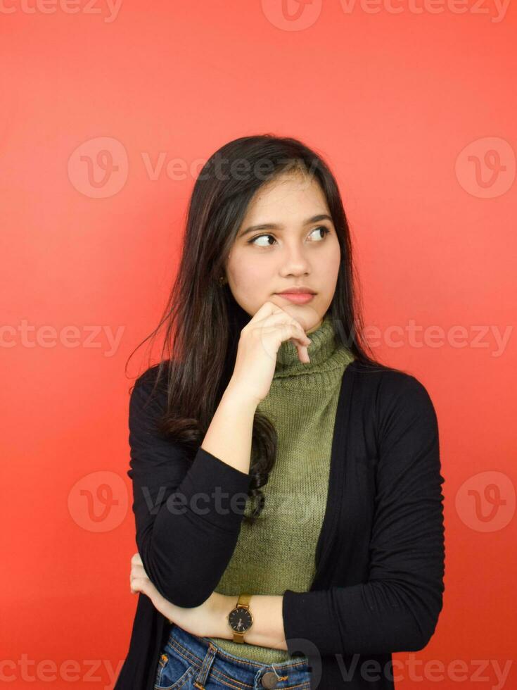 Hand on chin and doing thinking gesture Of Beautiful Asian Woman Isolated On Red Background photo