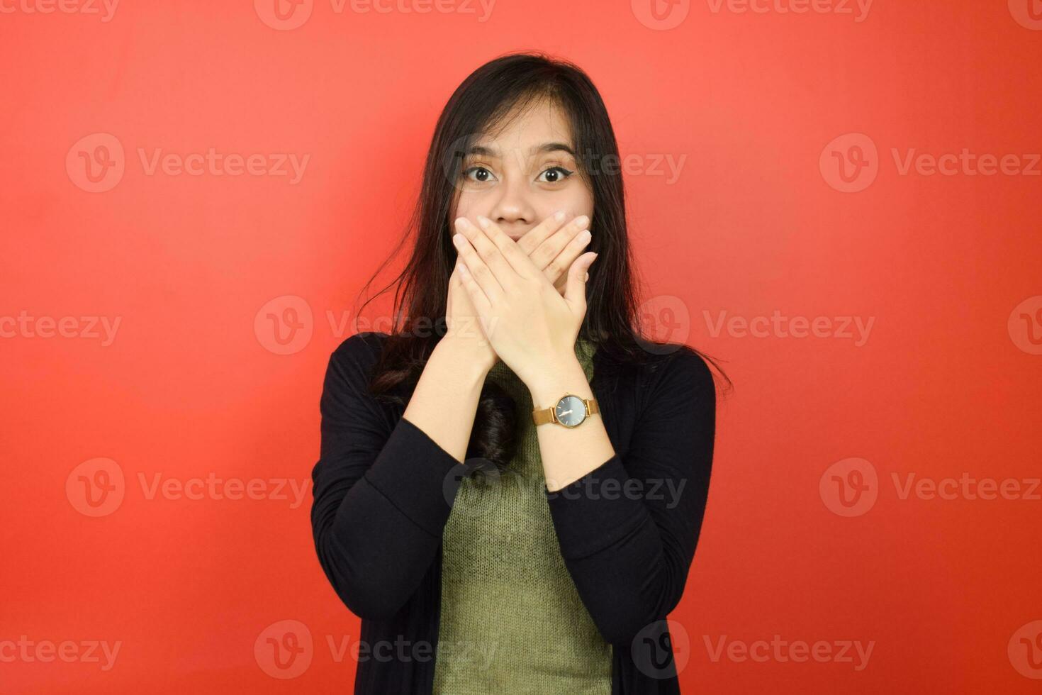Covering mouth with Shocked Face and Looking at Camera Of Beautiful Asian Woman Isolated On Red Background photo