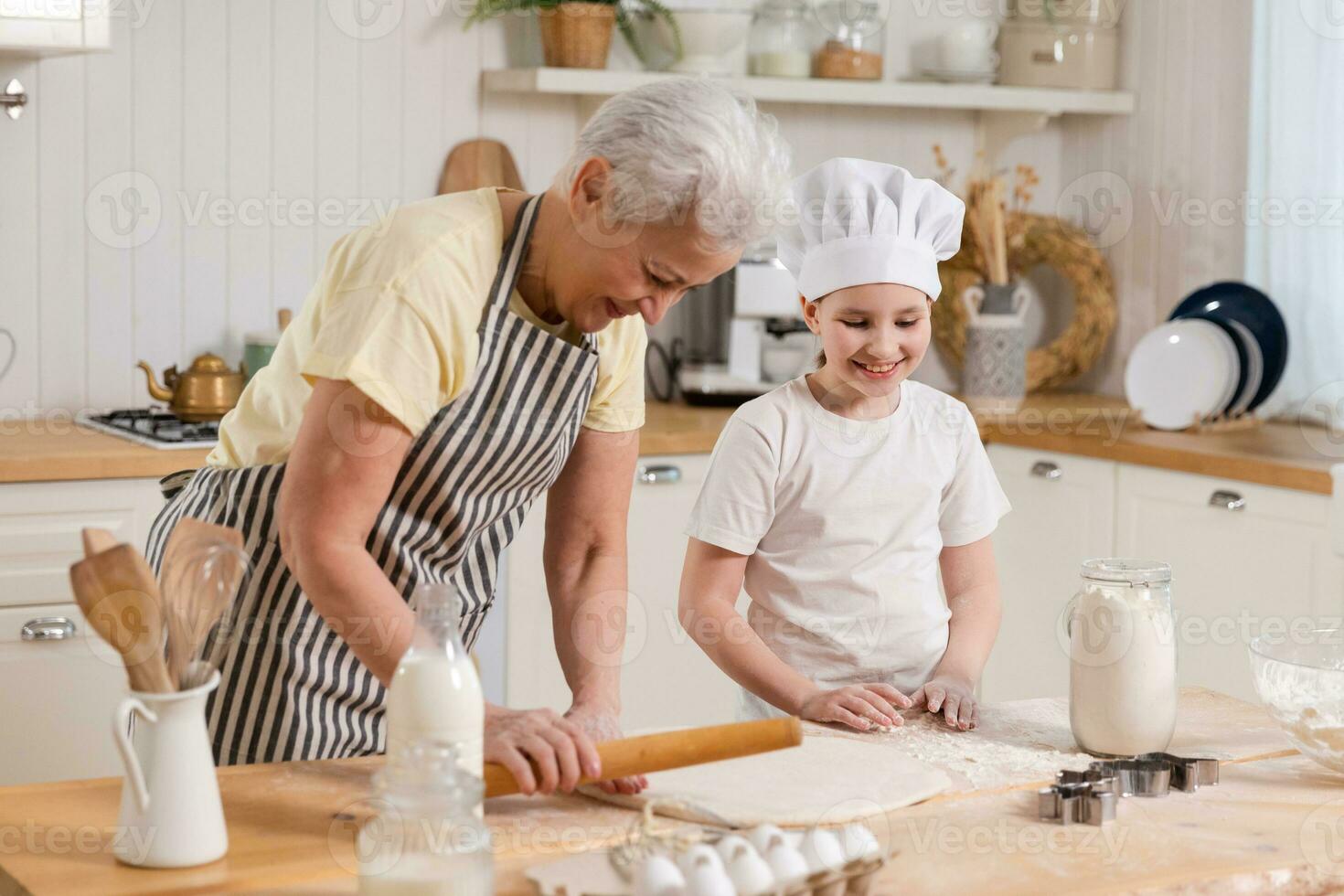 contento familia en cocina. abuela y nieta niño cocinar en cocina juntos. abuela enseñando niño niña rodar fuera masa hornear galletas. casa trabajo en equipo Ayudar familia generaciones concepto. foto