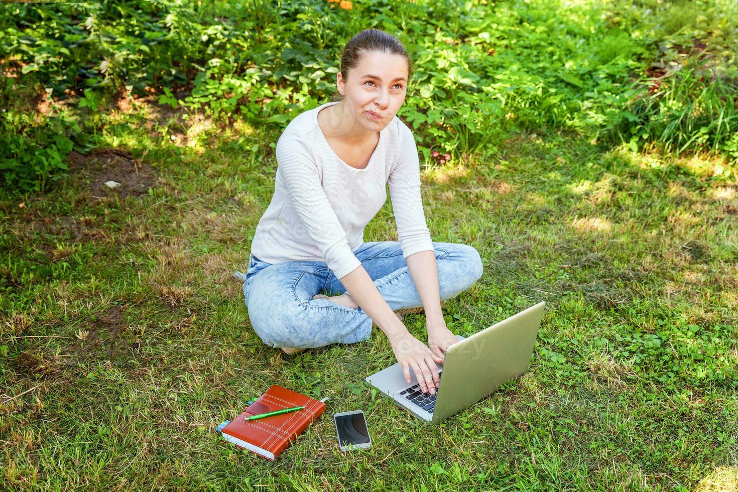 Young woman sitting on green grass lawn in city park working on laptop pc computer. Freelance business concept photo