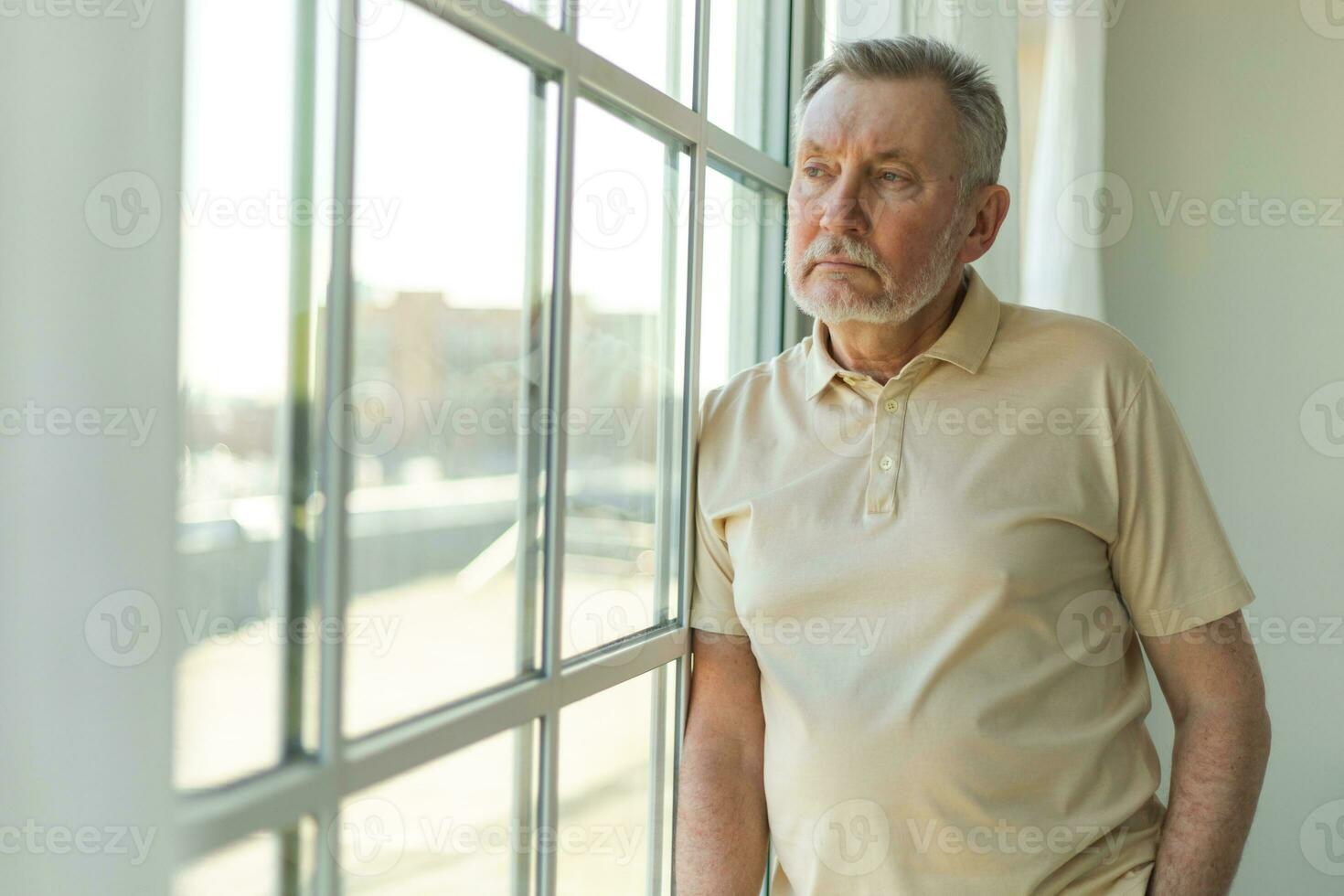 Sad tired lonely disappointed older senior man at home alone. Unhappy grandfather looking sadly outside window experiencing grief relative death bad news. Stressed elder man suffering from loneliness. photo