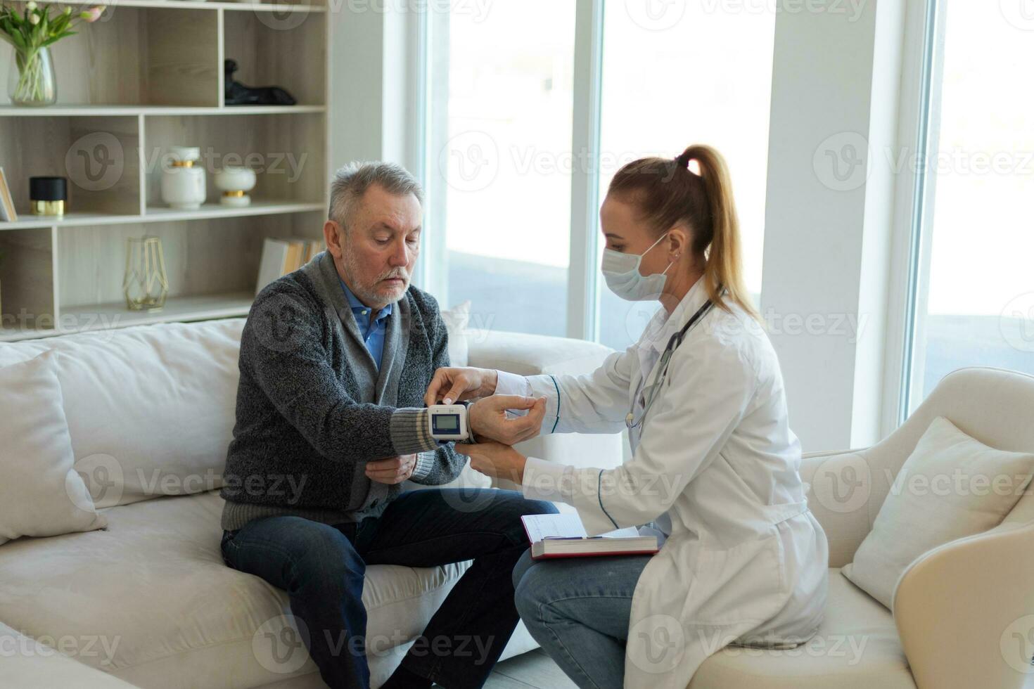 Female doctor senior man taking his blood pressure in doctor office or at home. Old man patient and doctor have consultation in hospital room. Medicine healthcare medical checkup. Visit to doctor. photo